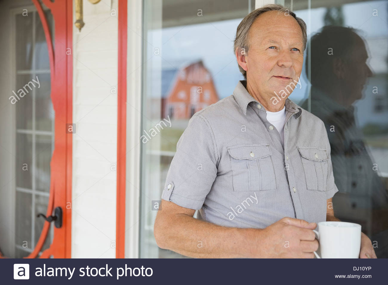 Hombre de pie en el porche senior con taza Foto de stock