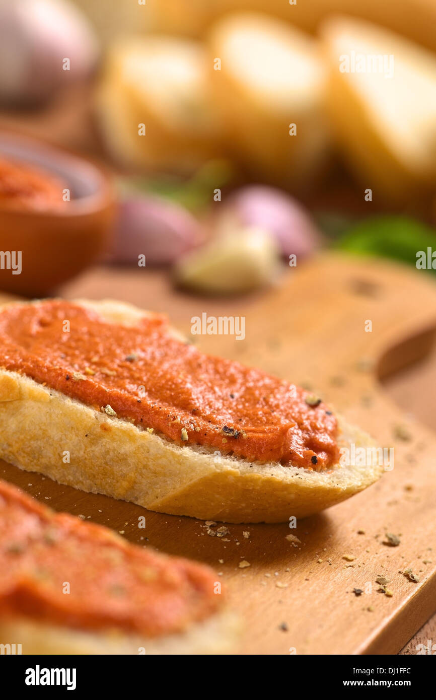 De tomate casera de mantequilla para untar en rodajas de pan baguette con pimienta molida fresca en placa de madera Foto de stock