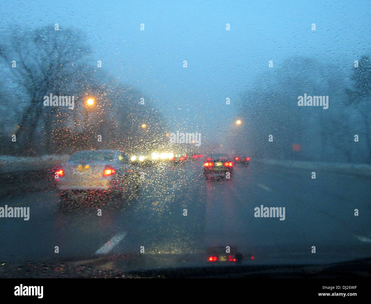 Conducir por una carretera al atardecer en la hora pico de tráfico con la lluvia y la niebla que se ciernen sobre el parabrisas. Foto de stock