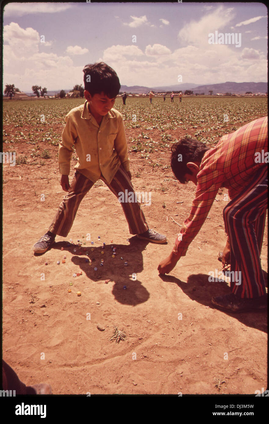 Los hijos de los trabajadores migrantes juegan canicas mientras sus padres trabajan en campos 855 Foto de stock