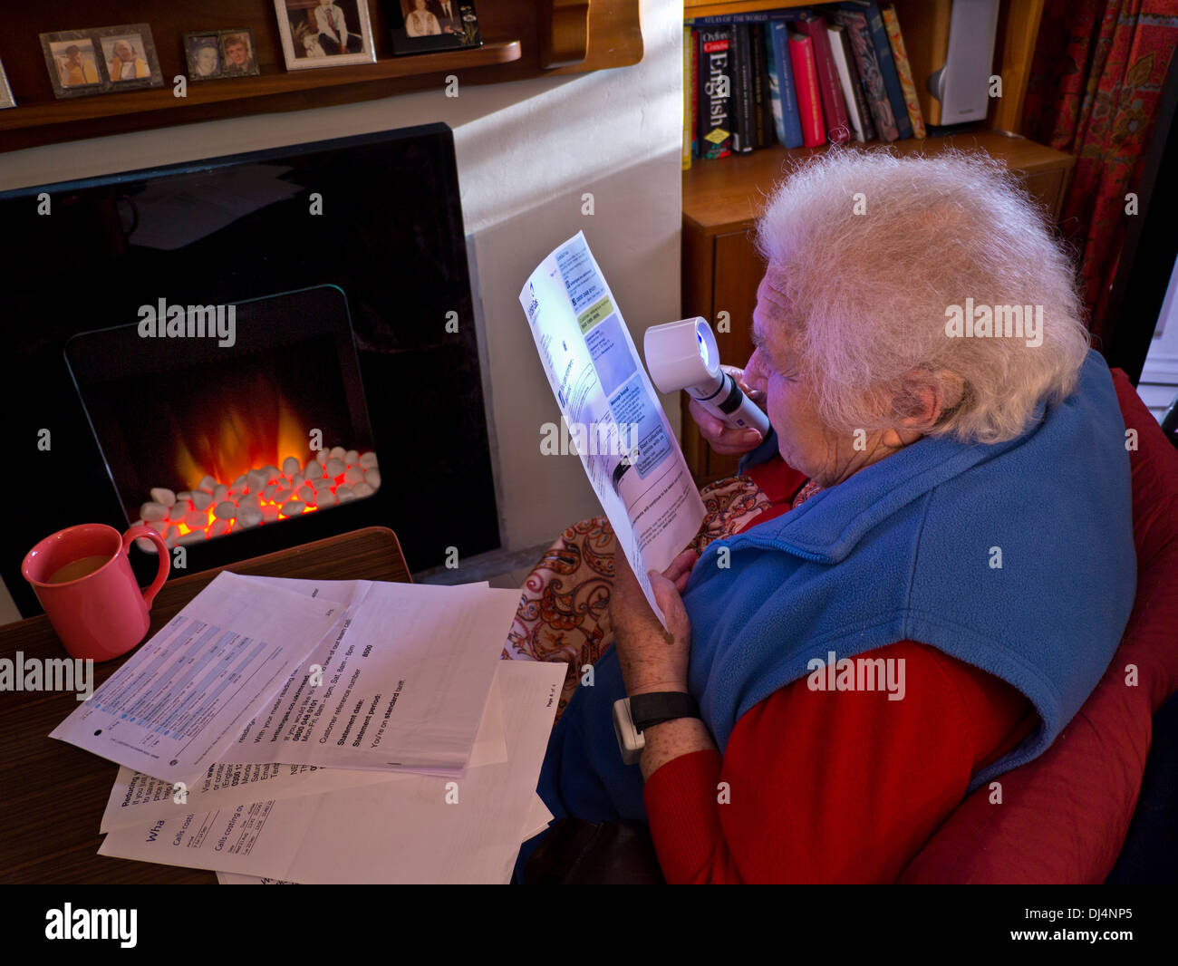 La energía de calefacción factura anciana independiente de 90s años dama en casa frente al fuego utilizando una lupa para leer sus últimas facturas de energía del hogar Foto de stock
