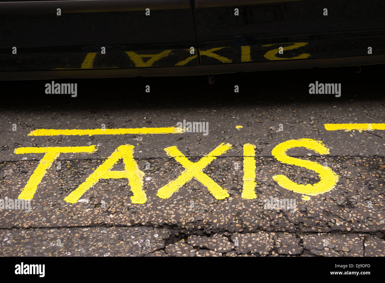 Una pintada de color amarillo del signo 'Taxi' sobre el asfalto se refleja en la puerta de un taxi negro de Londres. Foto de stock