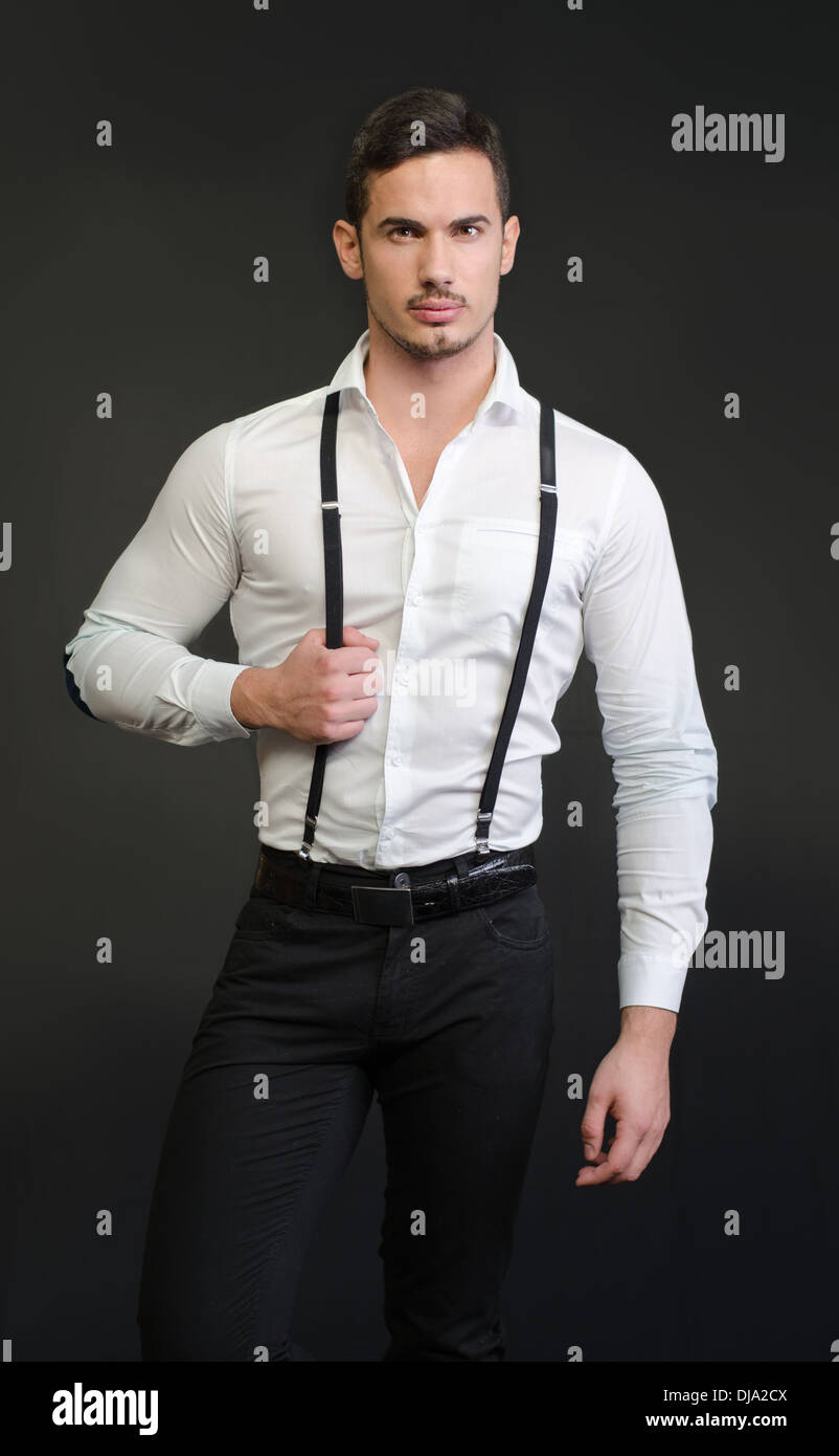 Joven elegante con camisa blanca y tirantes, en backgroung oscuro, serio, seguro stock - Alamy