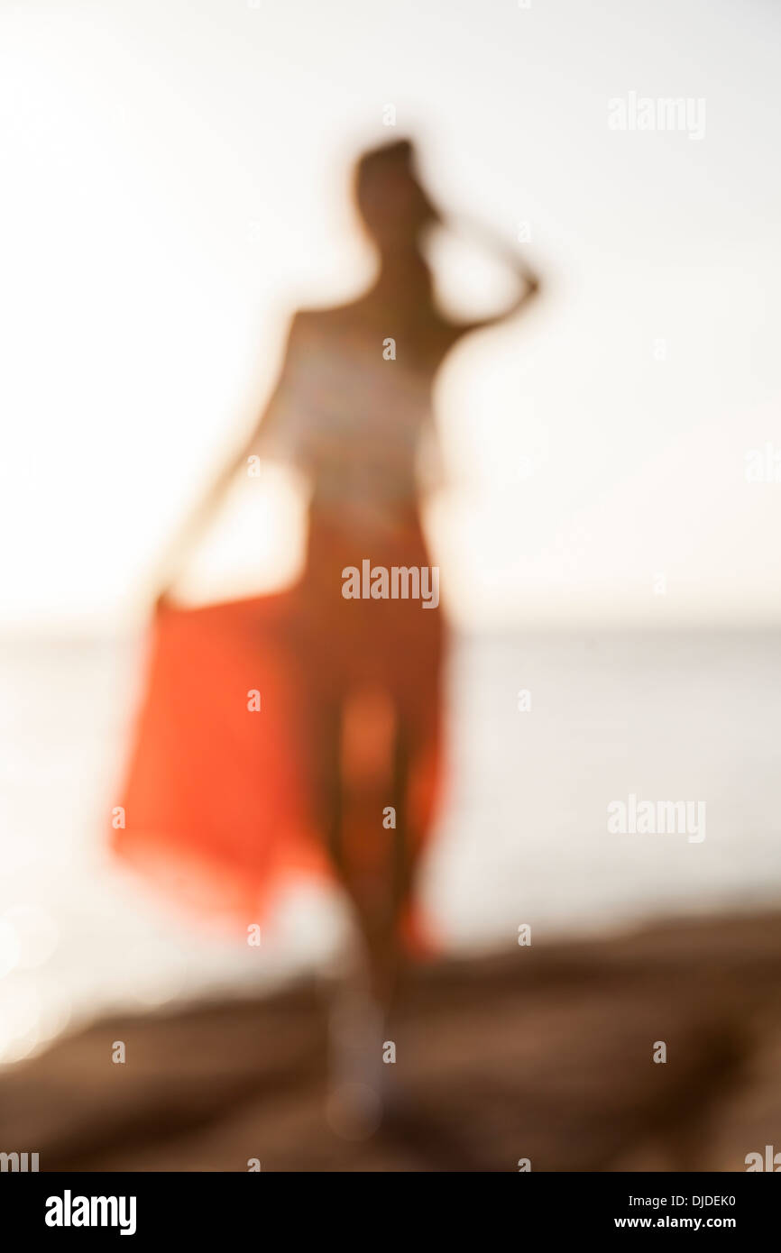 Fuera de foco borrosa la mujer en rojo de la falda y top blanco caminando sobre el acantilado con el mar y el cielo en segundo plano. Foto de stock