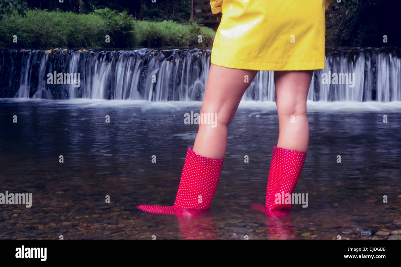 Mujer en amarillo impermeable y botas de goma roja mirando pintorescas cataratas Foto de stock
