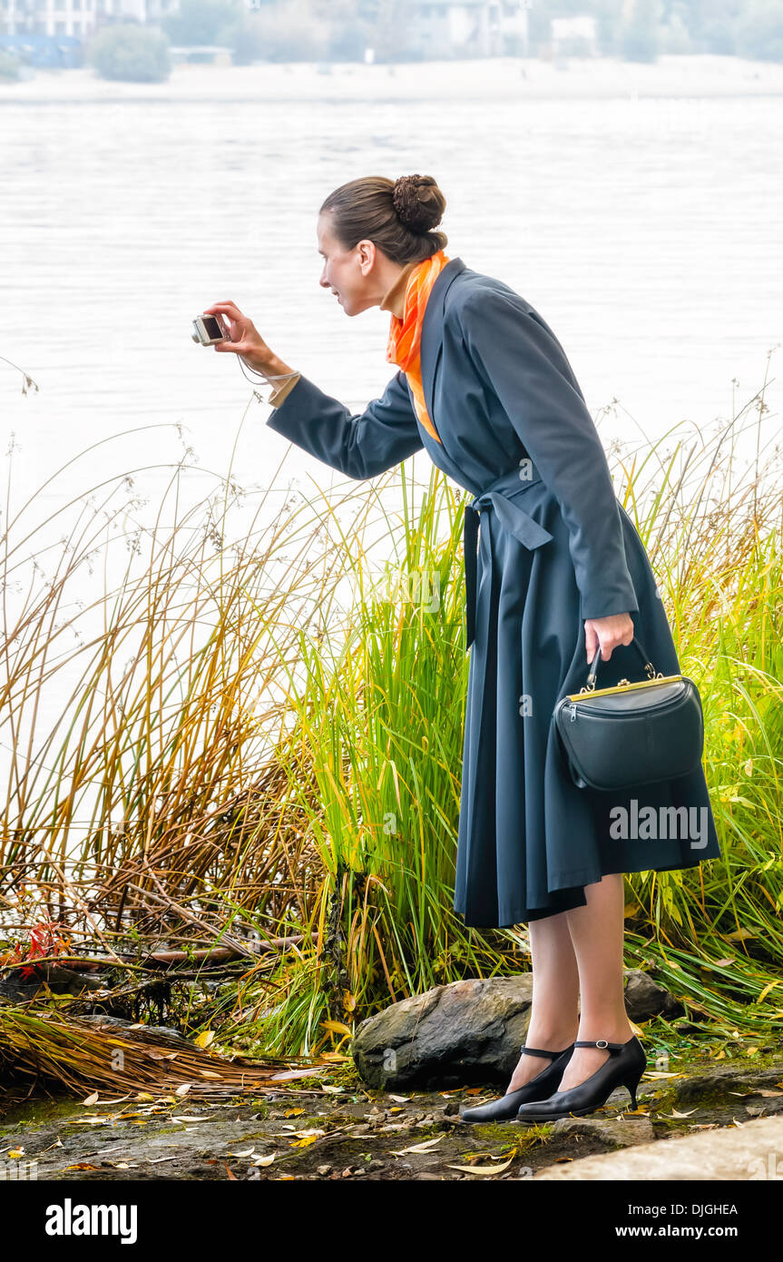 Senior elegante mujer de negocios con una cámara digital, un bolso y un pañuelo naranja, tomar fotos a lo largo del río Foto de stock