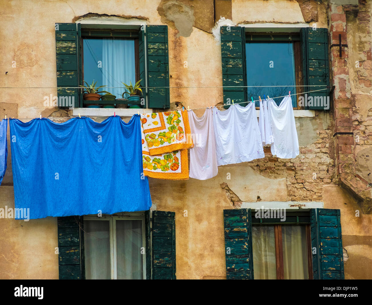 Servicio de lavandería de brillantes colores colgando sobre el lavado de línea entre ventanas con persianas, Venecia, Italia Foto de stock