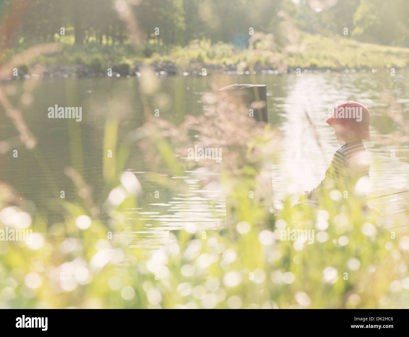 Momento en el estilo de vida del verano de la infancia. Niña sentada en embarcadero por canal, Suecia Foto de stock