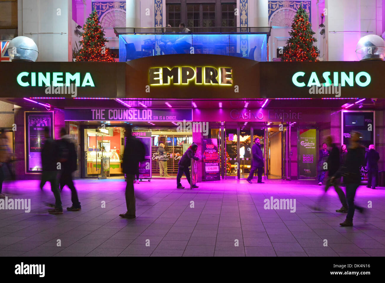 Personas en el pavimento fuera de Empire Leicester Square cine casino locales de entretenimiento cerise coloreado iluminación de inundación Londres, Inglaterra, Reino Unido Foto de stock