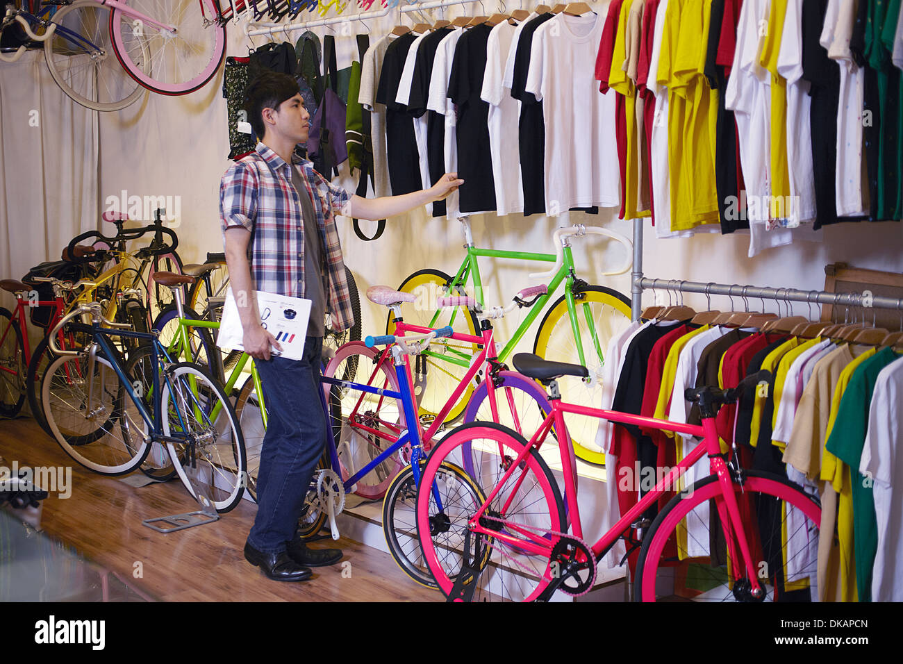 Joven en la tienda de bicicletas eligiendo camiseta Foto de stock