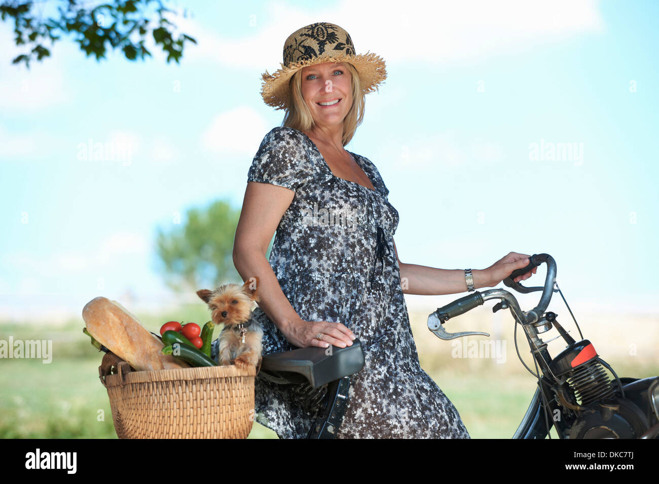 Mujer madura en bicicleta eléctrica con perro y hortalizas en la cesta Foto de stock