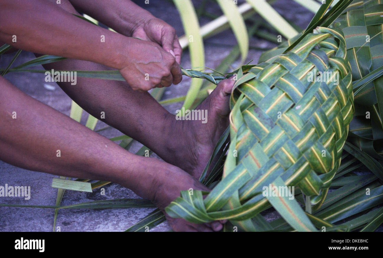 Una mujer Polinesia tejen canastos, empleando materiales de palma de coco. Foto de stock