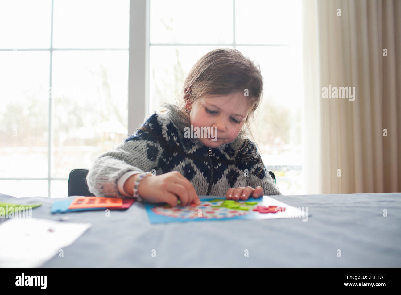 Muchacha sentada a la mesa, concentrándose en juego Foto de stock