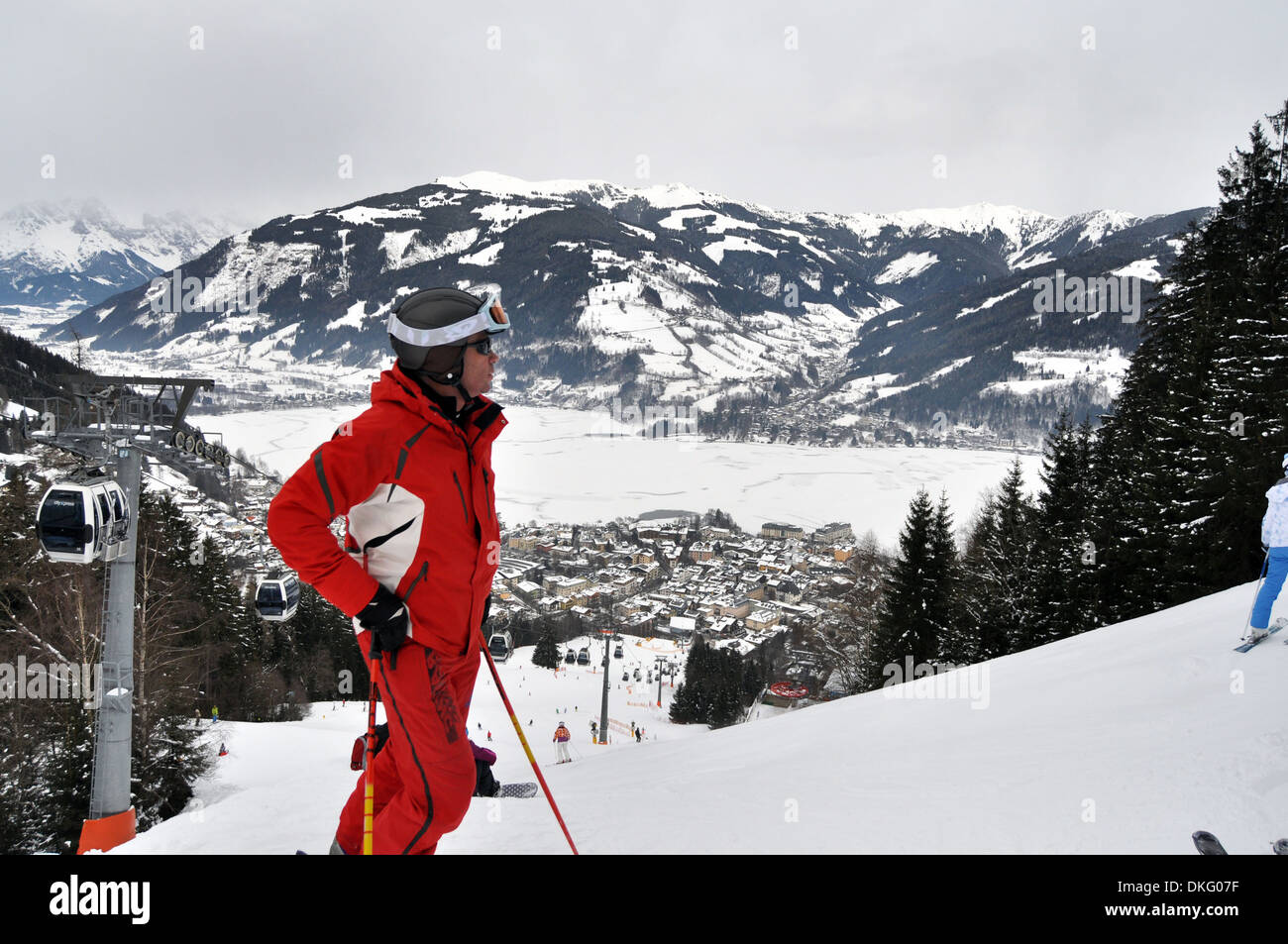 Hombre en un rojo brillante traje de esquí se encuentra en la parte superior de la pista, Zell am See, Austria Foto de stock