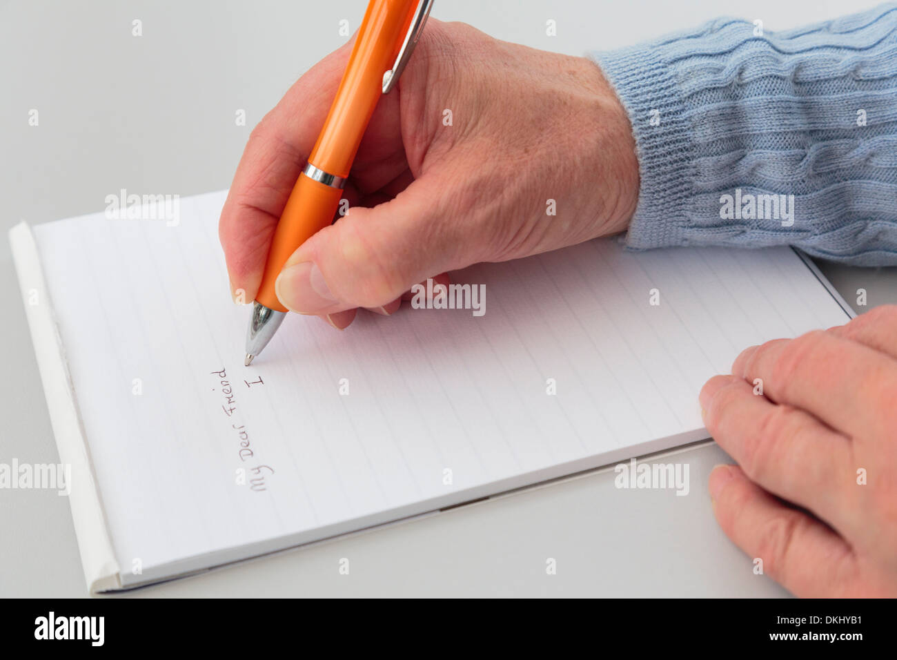 Una mujer mayor escribiendo una carta a un amigo con un bloc de papel sobre una mesa. Foto de stock