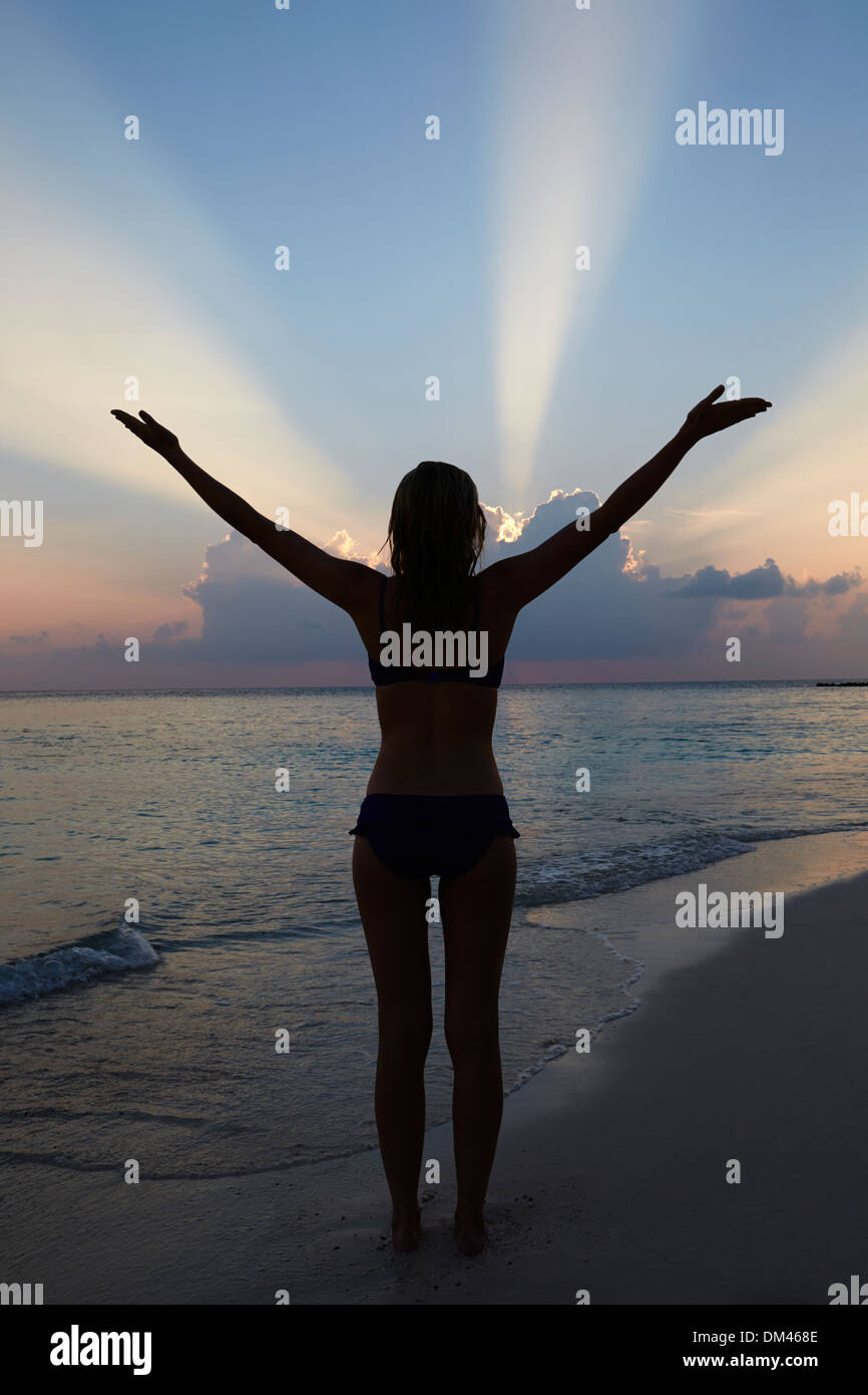 Silueta de mujer con los brazos estirados en la playa Foto de stock