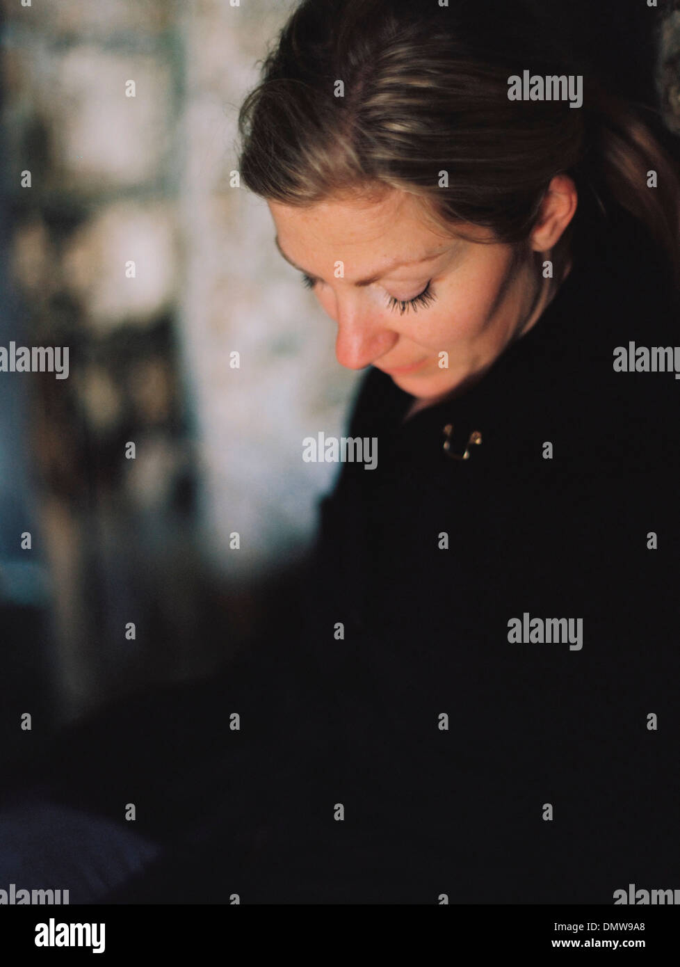Una mujer vistiendo un abrigo negro mirando hacia abajo en un estado de ánimo pensativo. Foto de stock