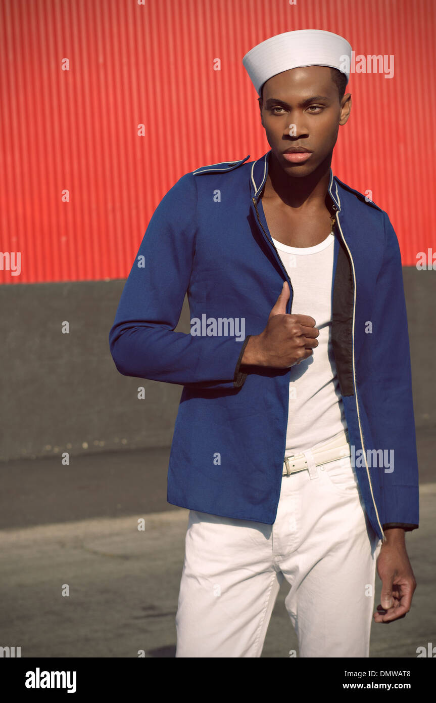 Guapo negro hombre vestido con un sombrero marinero chaqueta militar azul,  blanca y pantalón posando con rojo en la pared del fondo Fotografía de  stock - Alamy