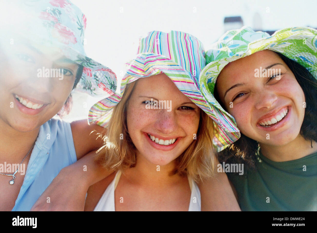 Tres chicas jóvenes en una fila vistiendo gorros para el sol mirando a la cámara y sonriendo. Foto de stock