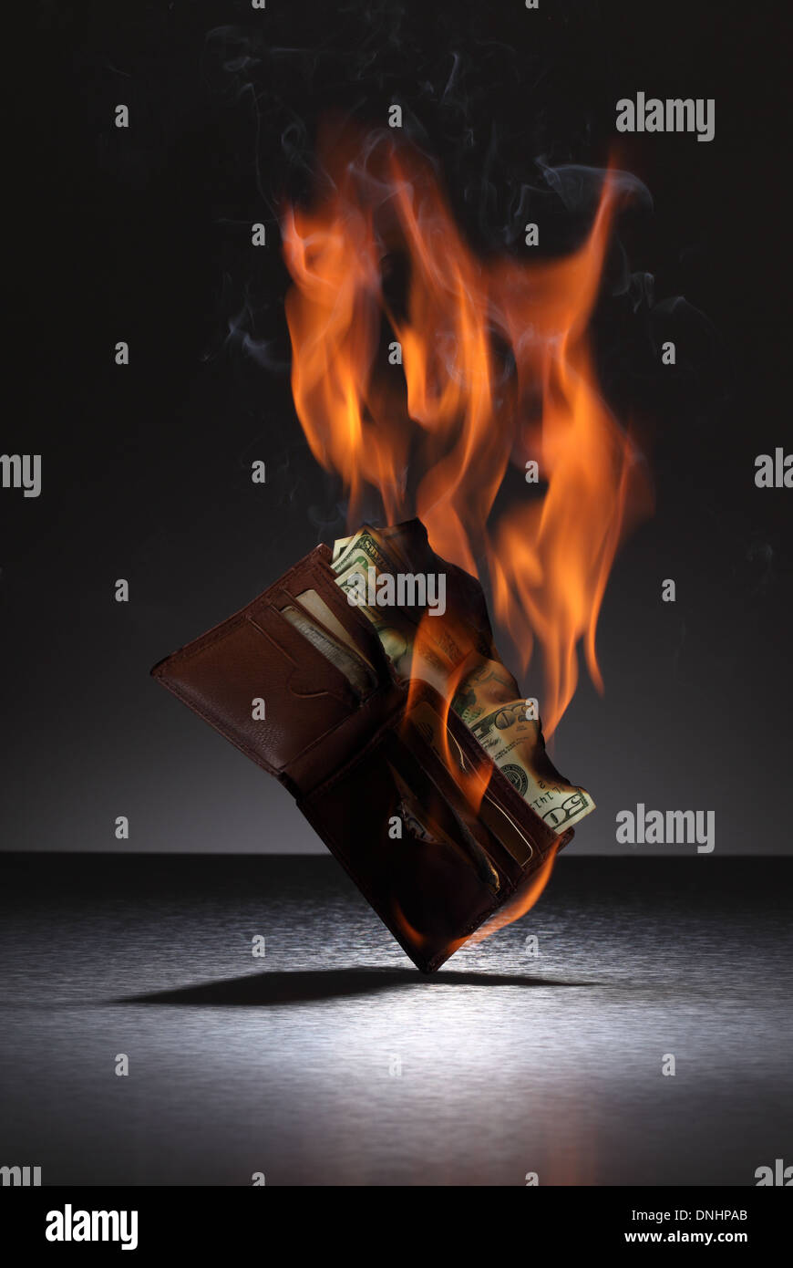 Una cartera de cuero marrón llena de tarjetas de crédito y dinero en fuego. Foto de stock