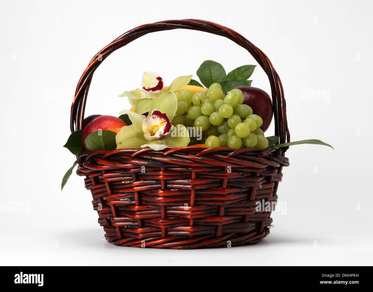 Una cesta llena de frutas variadas sobre un fondo blanco. Foto de stock