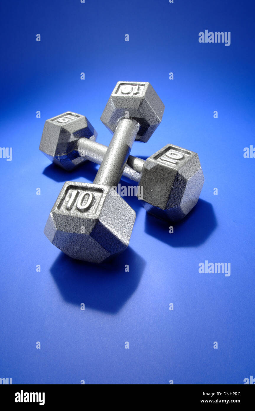 Un par de ejercicios de pesas metálicas sobre una colchoneta de ejercicios azul. Foto de stock