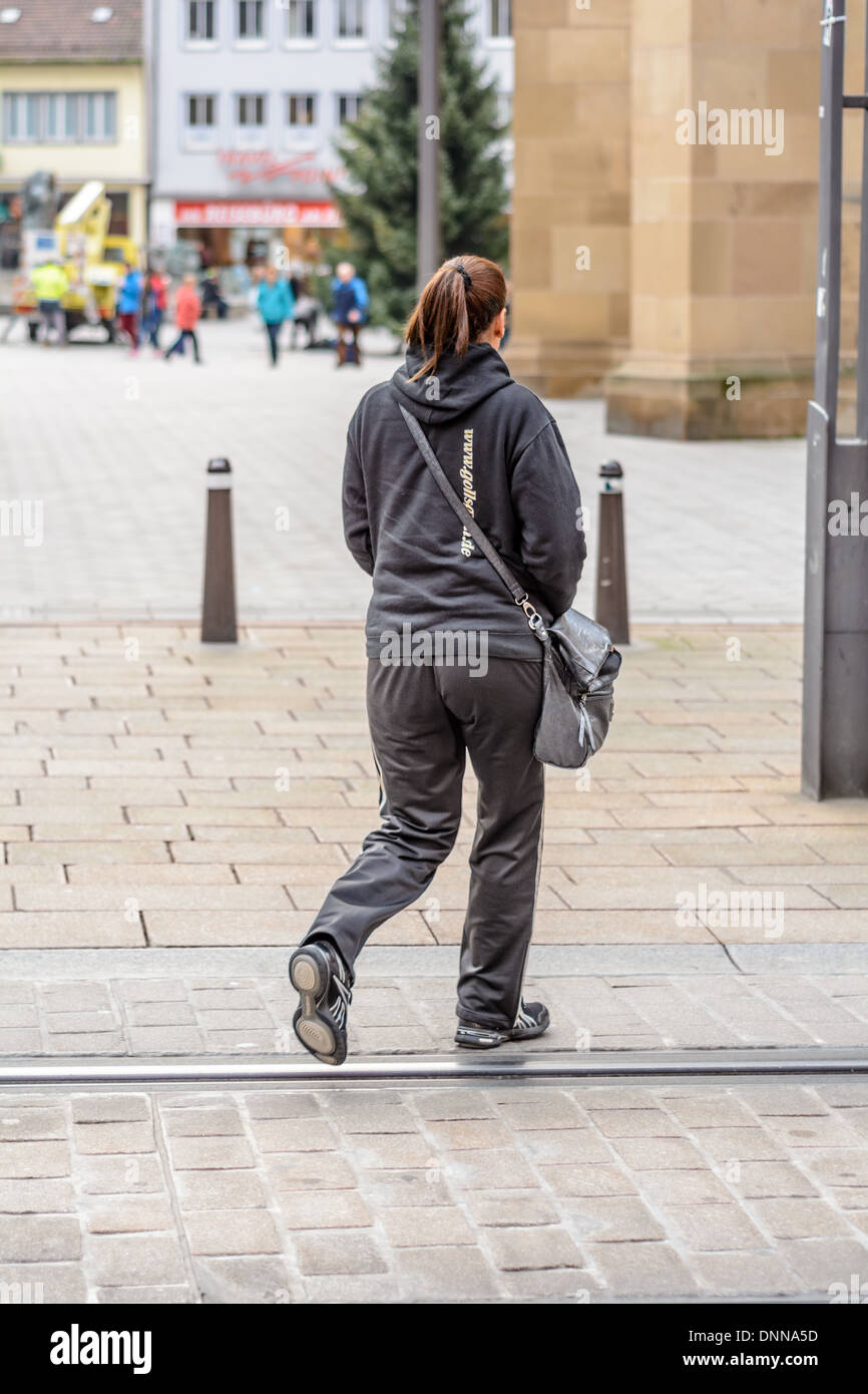 Joven mujer caucásica con pelo marrón hecho en una coleta vestido con traje  deportivo Adidas negro cruza una calle con rieles de empotramiento  Fotografía de stock - Alamy