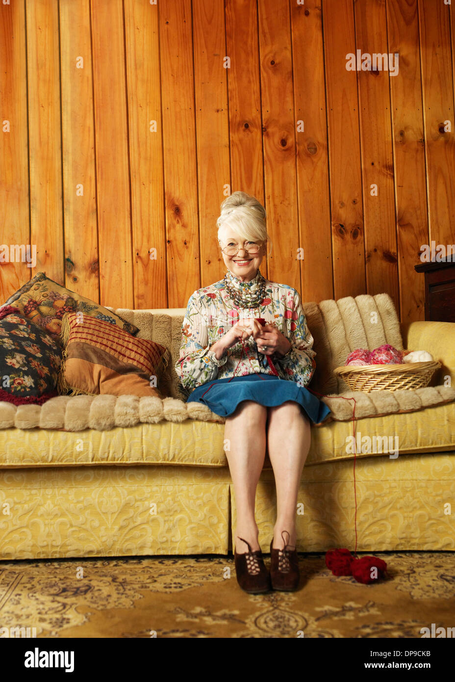 Retrato de mujer senior feliz tejiendo en el sofá en casa Foto de stock