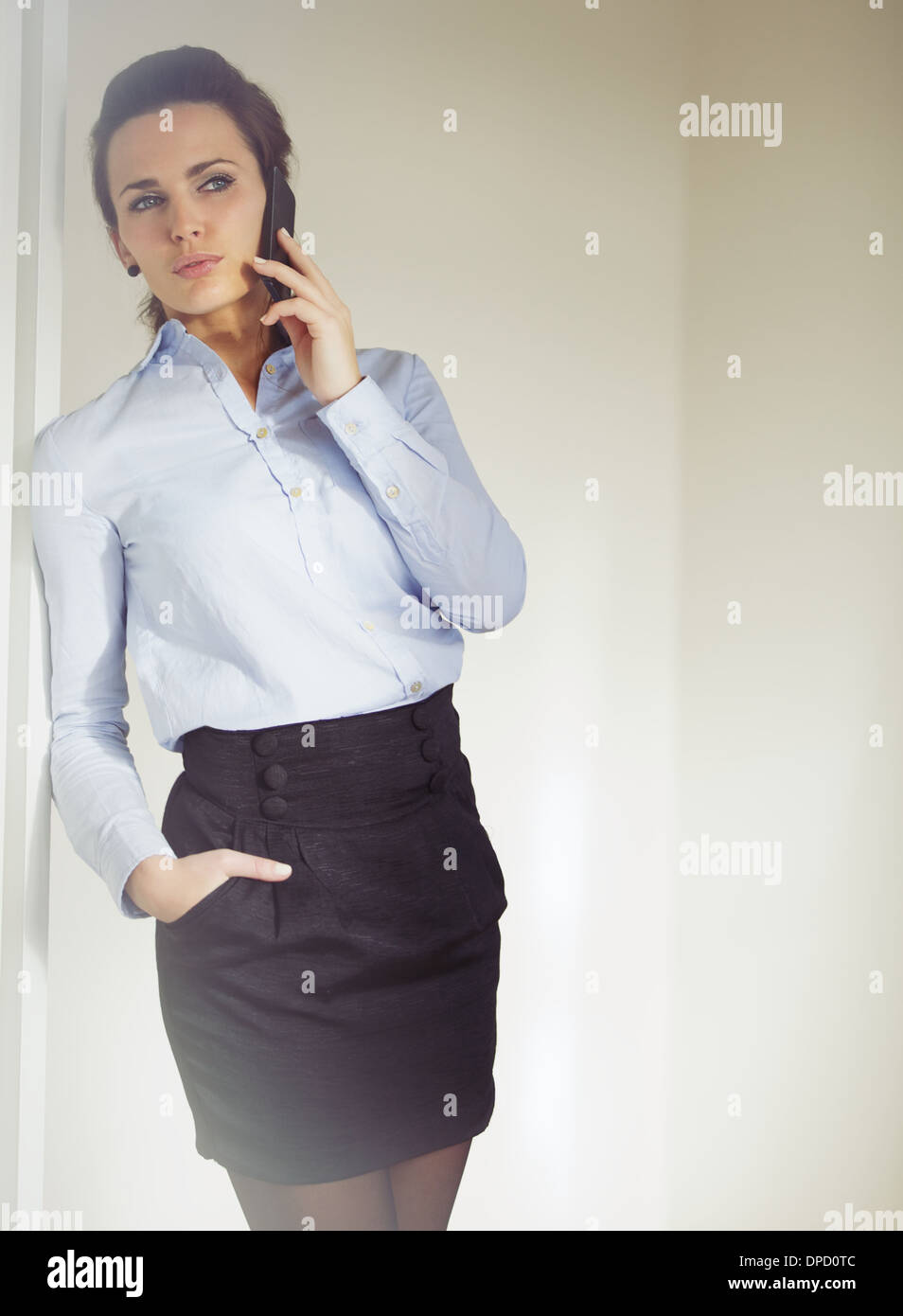 Elegante empresaria vestida con falda y camisa habla de negocios por teléfono. Mujer caucásica en los 20s Foto de stock