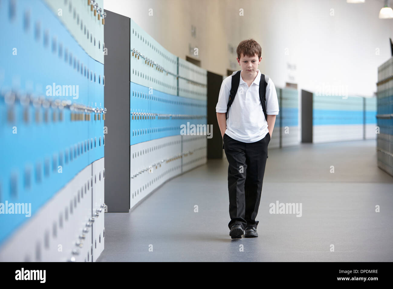 Infeliz colegial caminar solo en el corredor de la escuela Foto de stock
