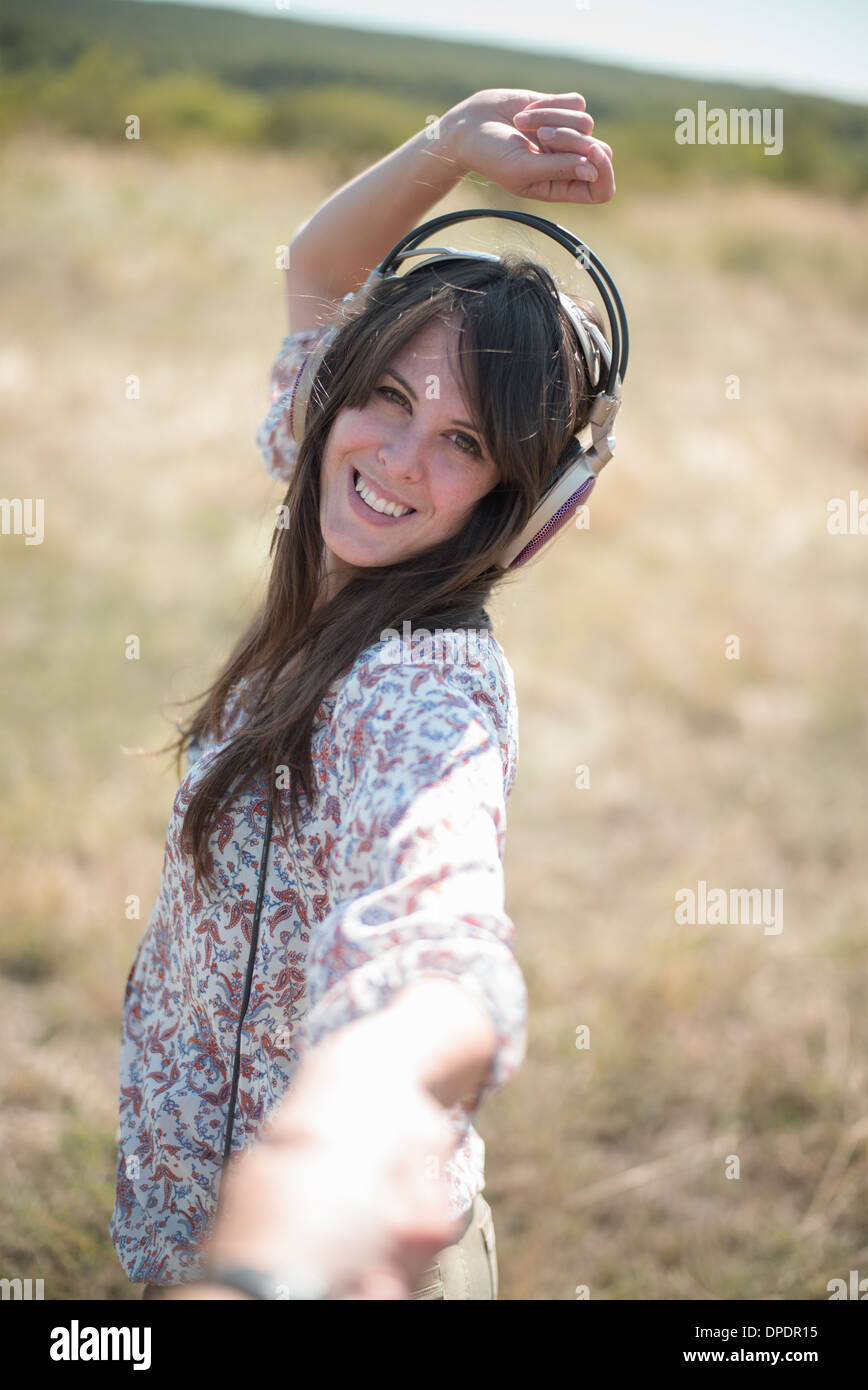 Retrato de mujer adulta media bailando en el campo con los brazos levantados, usando audífonos Foto de stock