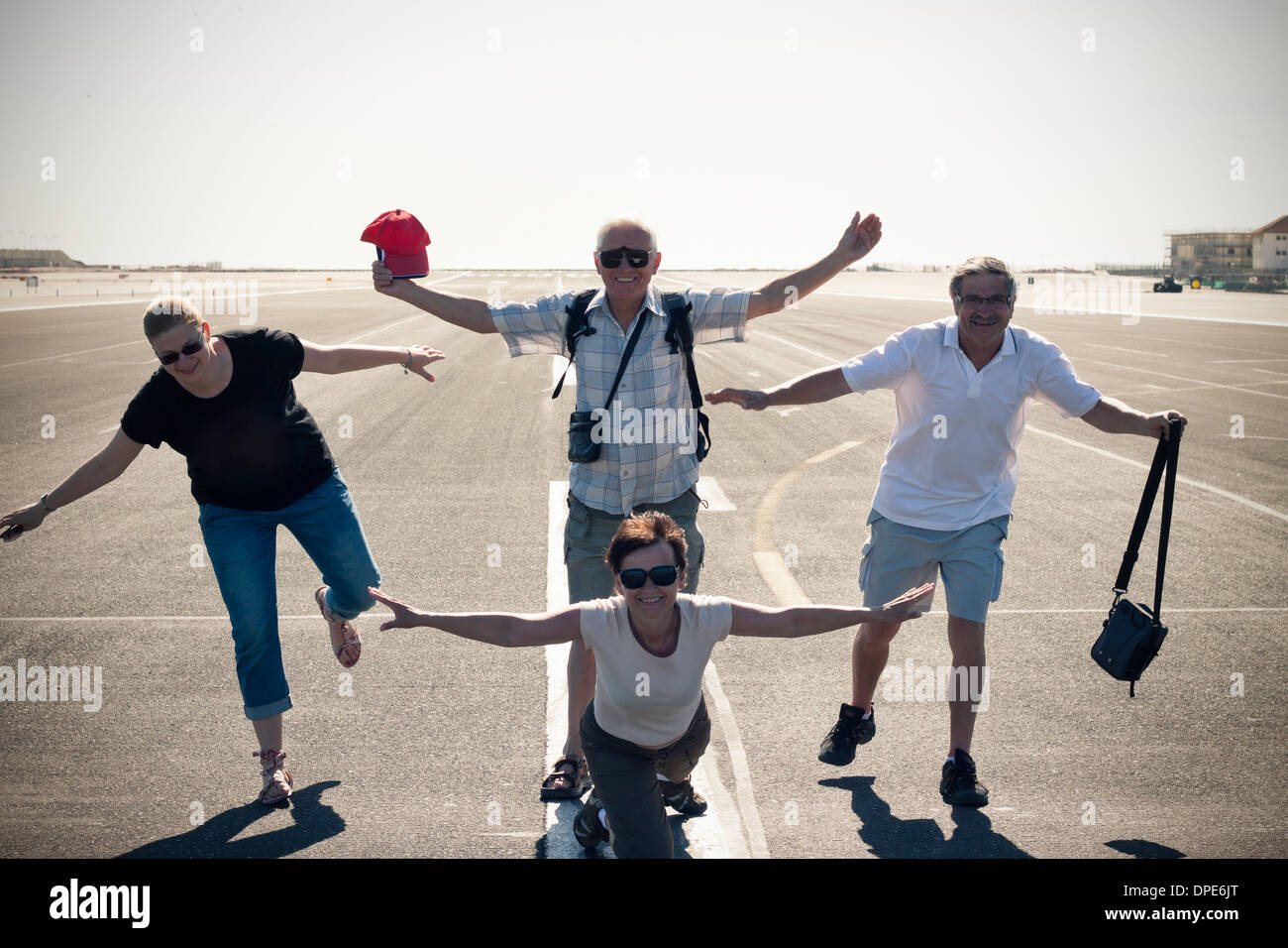 Divertido grupo de turistas imitando el avión en la pista del aeropuerto. Foto de stock