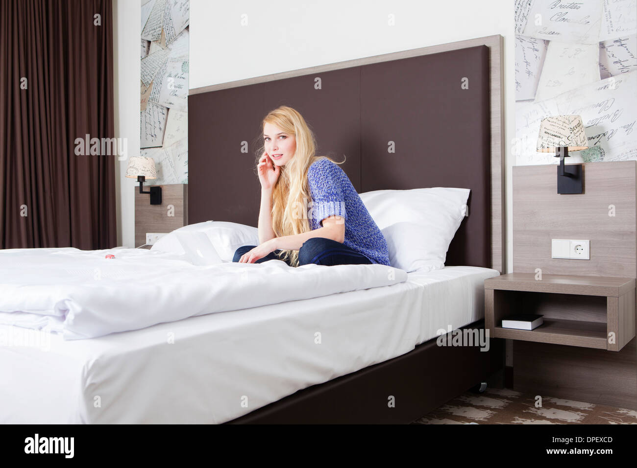 Mujer sentada con su portátil en la cama en una habitación de hotel Foto de stock