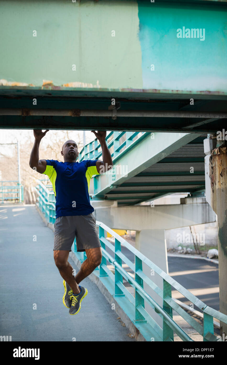 Hombre haciendo tirar ups en el puente Foto de stock