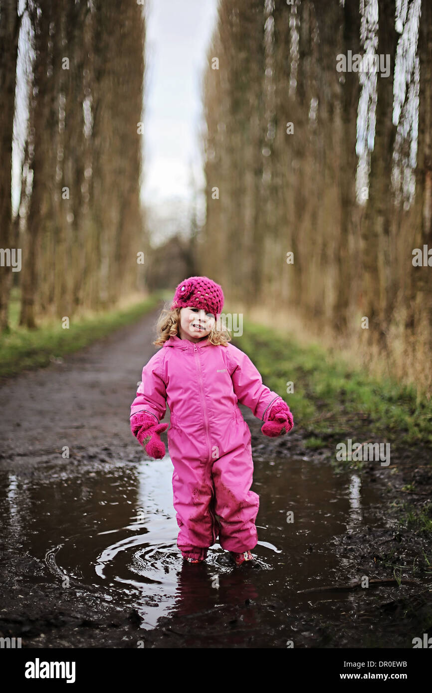 Niña de pie en charco en ruta arbolada vestidos de rosa. Foto de stock