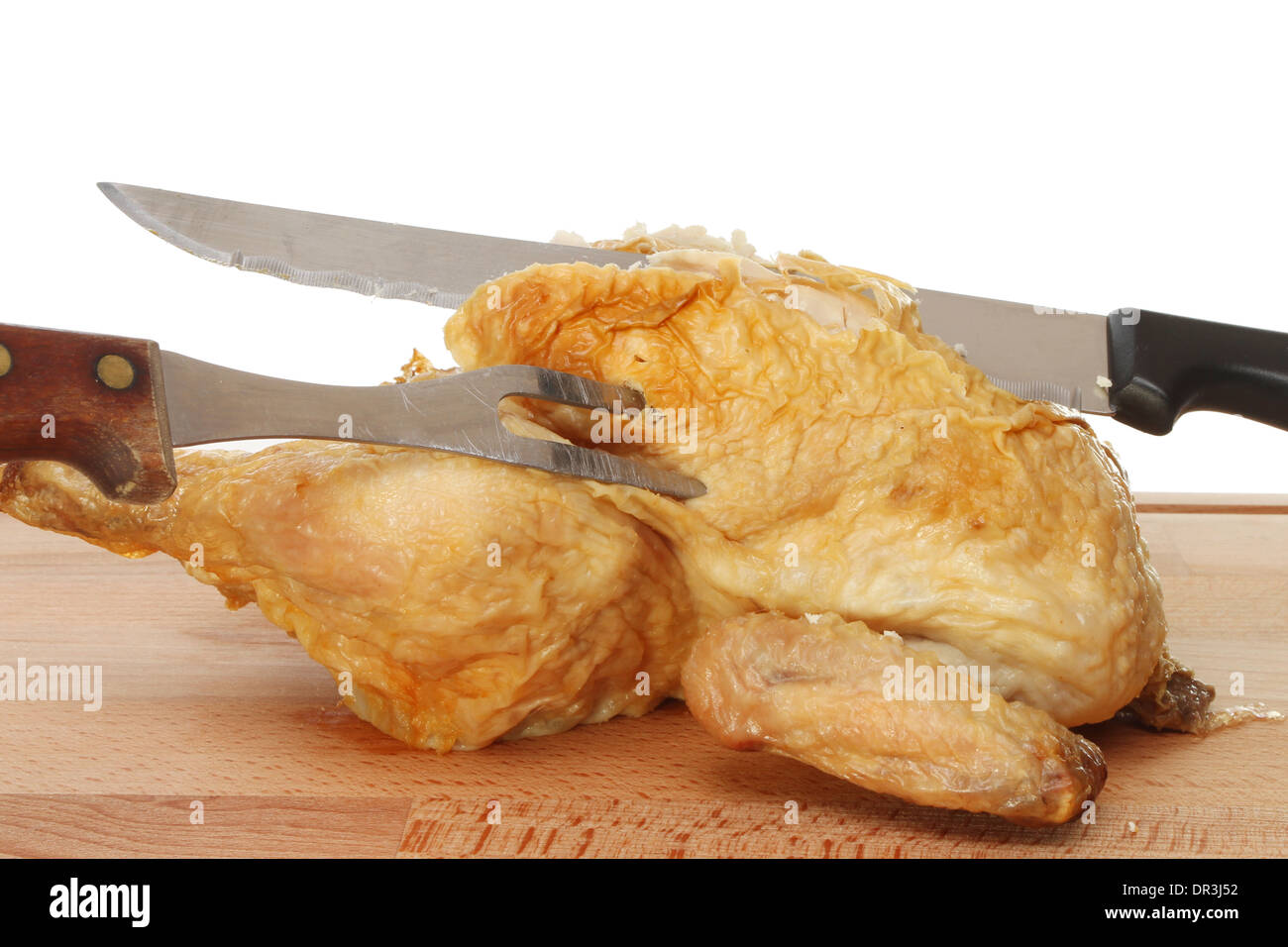 Pollo asado con un cuchillo y tenedor tallado sobre una tabla de madera Foto de stock
