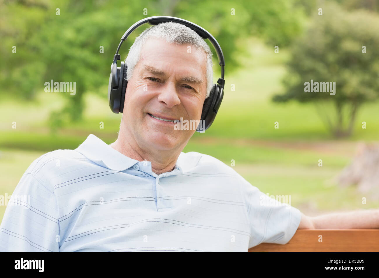 Hombre senior sonriente con auriculares en el parque Foto de stock