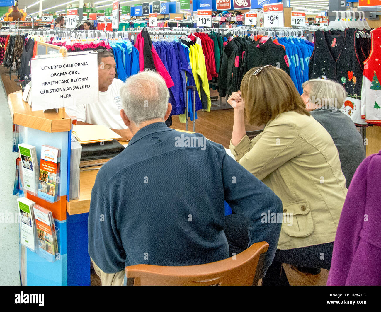 Un agente de seguros asesora a sus clientes en un quiosco de venta en una Laguna Niguel, CA, tienda de ropa de descuento ofreciendo cobertura en virtud de la Ley de salud asequible o Obamacare, conocida en el estado como cubiertas de California. Nota firmar y folletos. Foto de stock