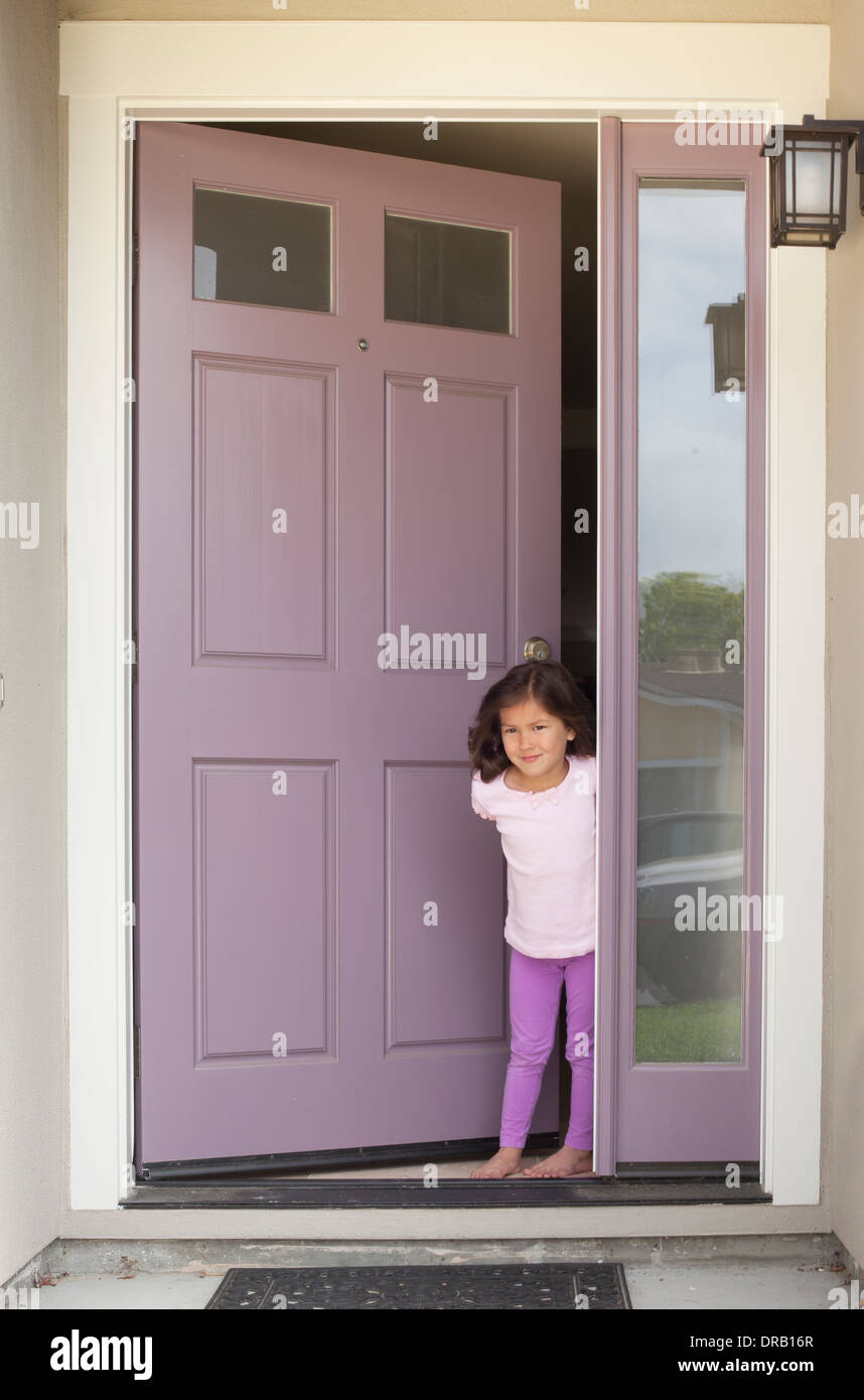 Niña con la puerta abierta a la entrada de la casa Foto de stock