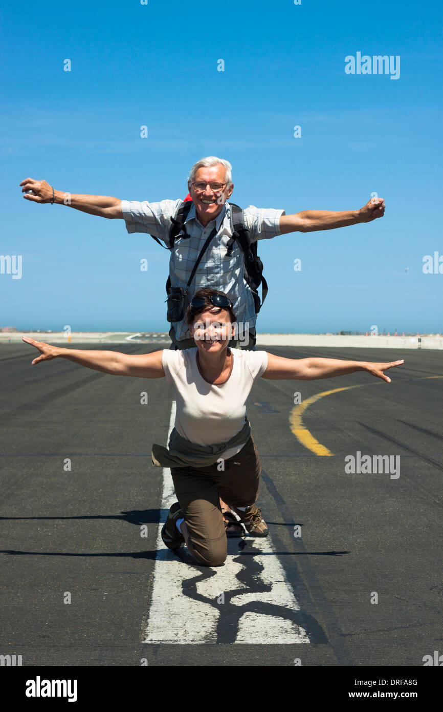 Feliz senior hombre y mujer de mediana edad imitando el avión en la pista de aterrizaje del aeropuerto Foto de stock