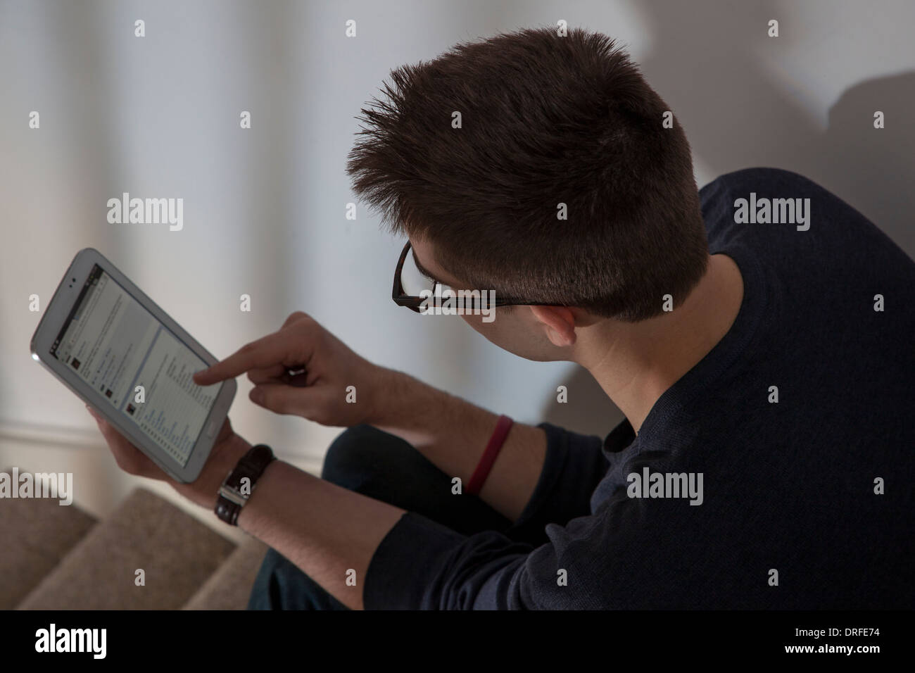 Sobre el hombro foto de hombre con gafas ver un sitio web de redes en la pantalla táctil de Tablet digital. Foto de stock