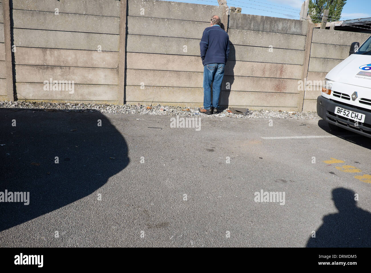 Hombre mirando a través de la grieta en la valla de hormigón espiar Foto de stock