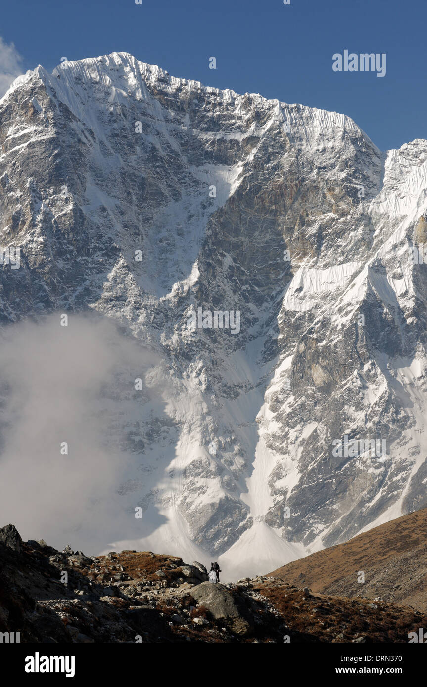 La diminuta figura de un caminante es eclipsado por la cara oriental de Taboche en el campamento base del Everest trek Foto de stock