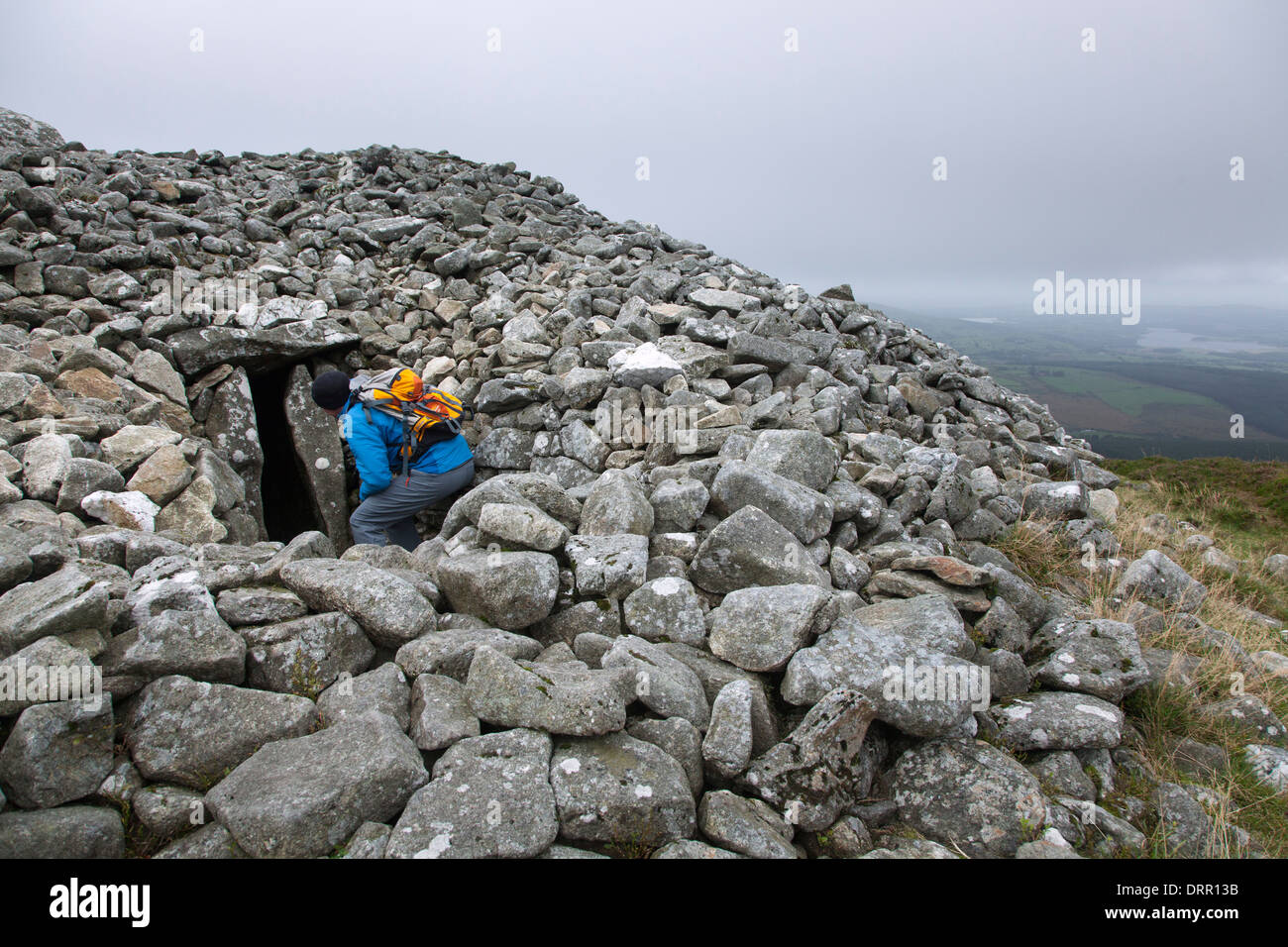 Walker examina la entrada a una tumba del neolítico en la cumbre de Seefin (621m), montañas de Wicklow, en el Condado de Wicklow, Irlanda. Foto de stock