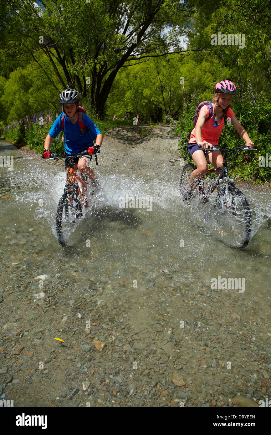 Los ciclistas de montaña cruzando por la corriente del río Arrow, Flecha Río puentes Ride, Arrowtown, Otago, Isla del Sur, Nueva Zelanda Foto de stock