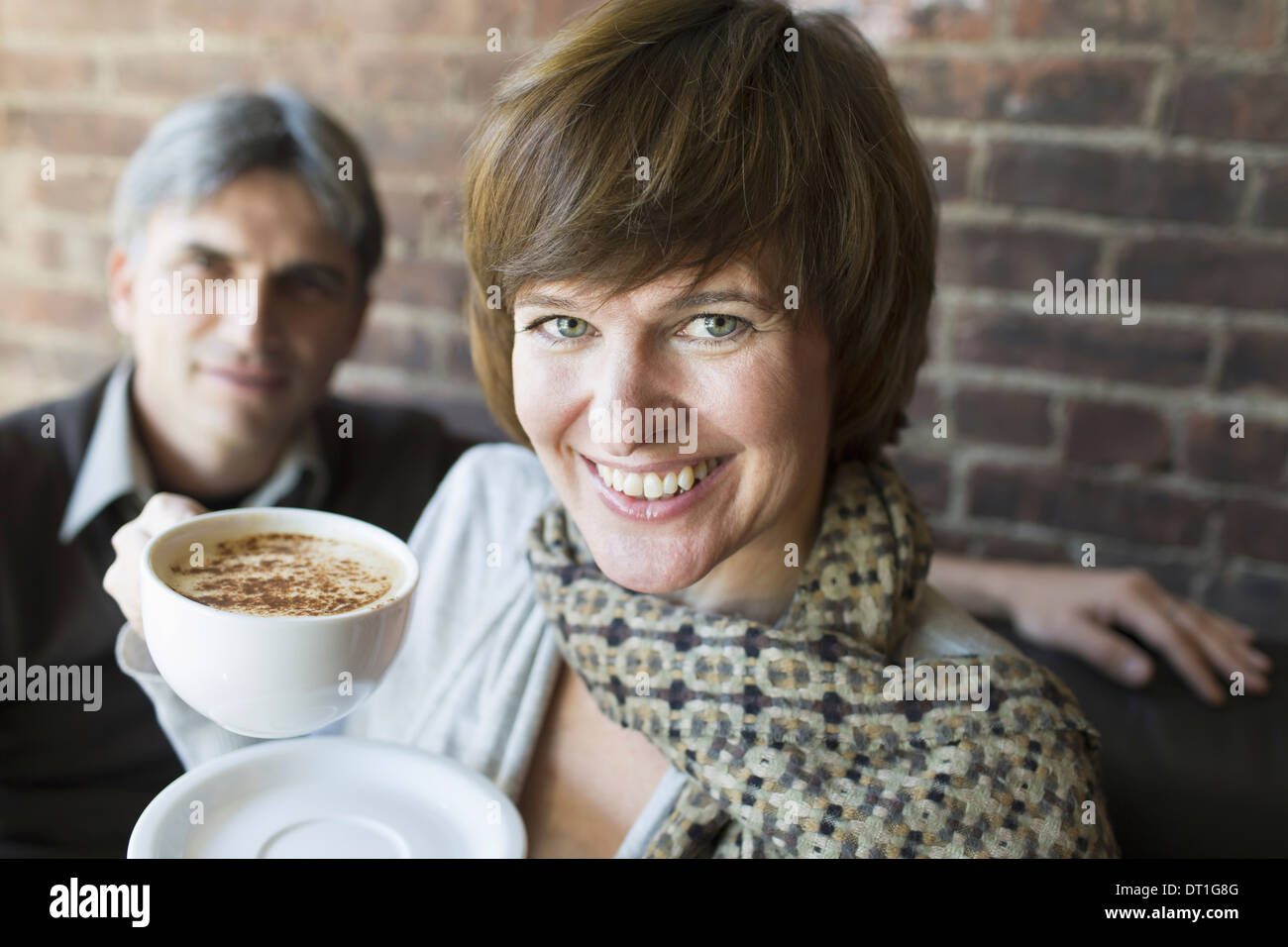 Dos personas sentadas en una cafetería, un hombre y una mujer sosteniendo china blanco tazas de café cappuccino Foto de stock