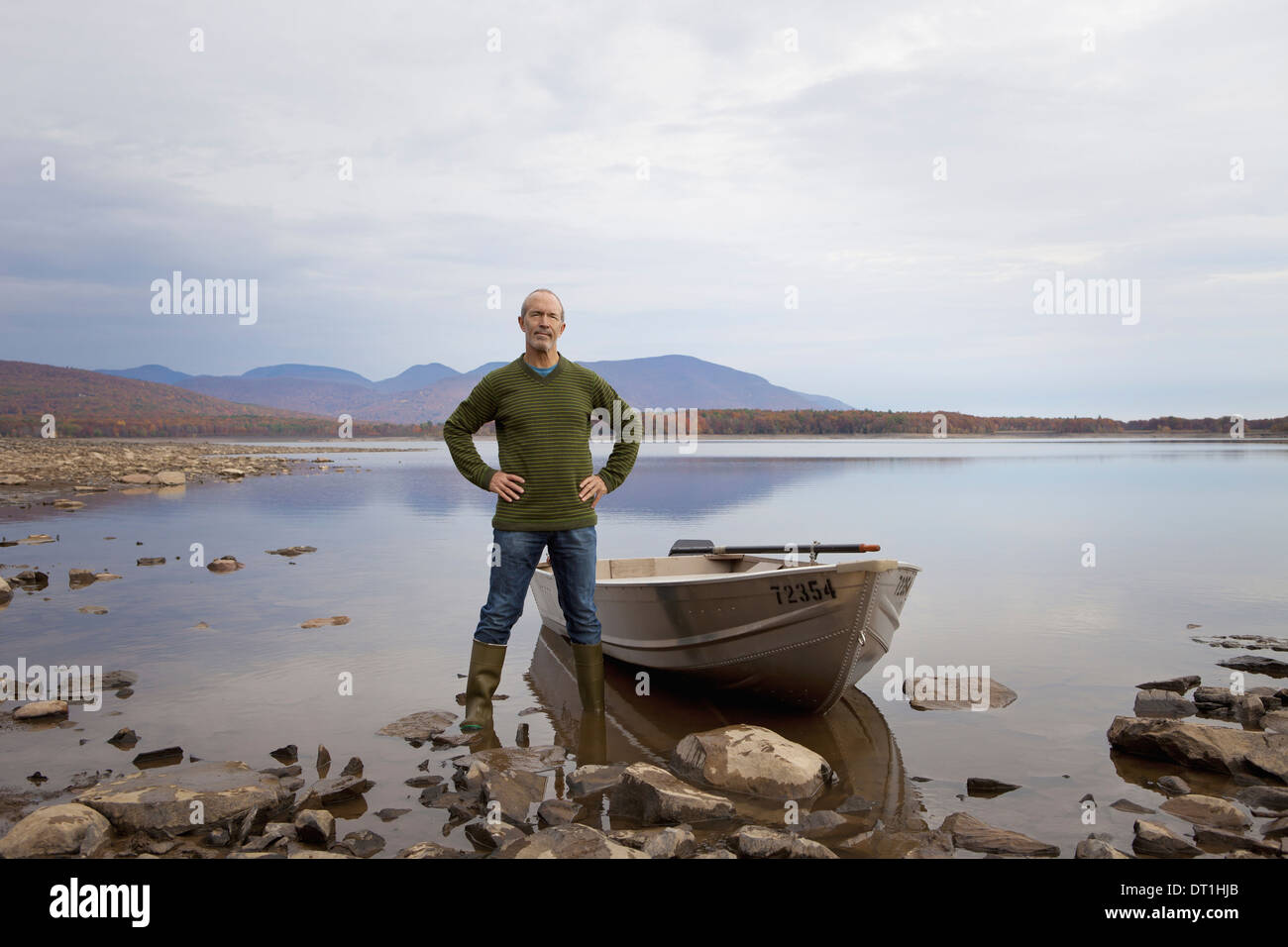 Un hombre de pie sobre un lago al lado de un pequeño bote a remo Foto de stock