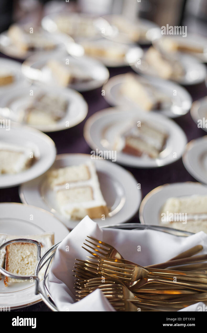 Una tabla cargados con placas blancas y china una canasta llena de horquillas de postre una rebanada de pastel de boda Foto de stock