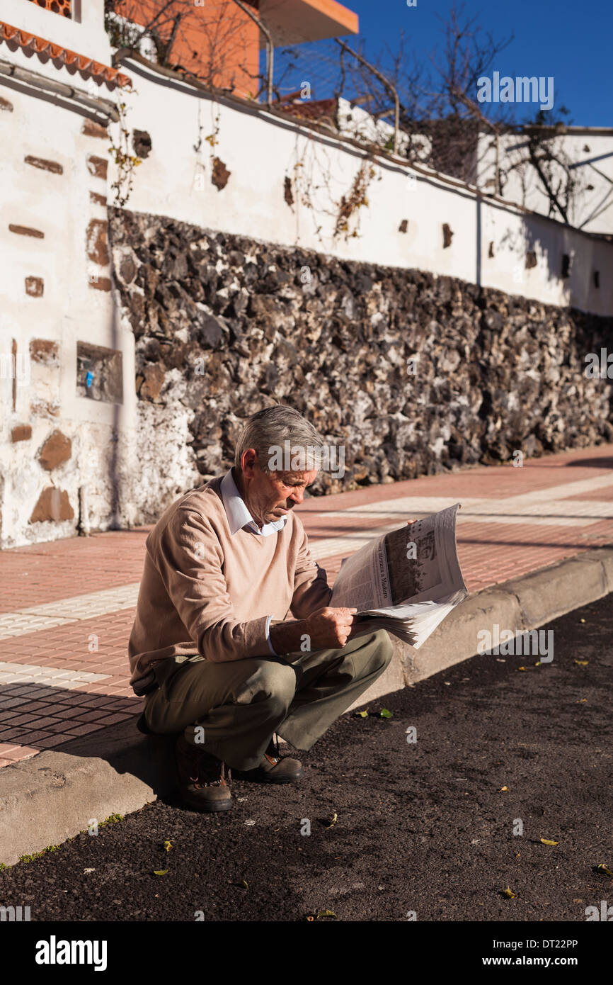 Hombre sentado en frenar leyendo el periódico matutino en Arguayo, Tenerife, Islas Canarias, España. Foto de stock