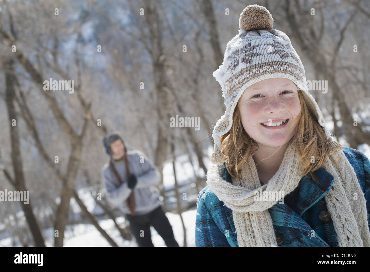 Paisaje invernal con nieve en el suelo una joven con un bobble sombrero y bufanda al aire libre, a un hombre en el fondo Foto de stock